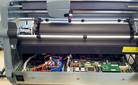 Une imprimante professionnelle grand format aussi appelée traceur est ouverte, ses circuits et fils bien visibles.