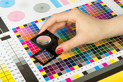 Une main de femme passe une loupe sur un tableau indiquant les nombreux profils de couleur d'imprimante.